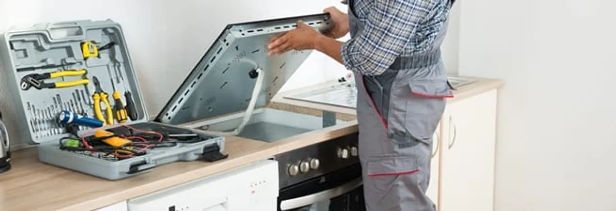 Cooktop repair technician lifting a built-in stovetop for service in Detroit, MI