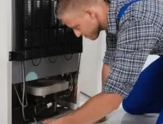 Refrigerator repair technician servicing the compressor and condenser area in Detroit, MI